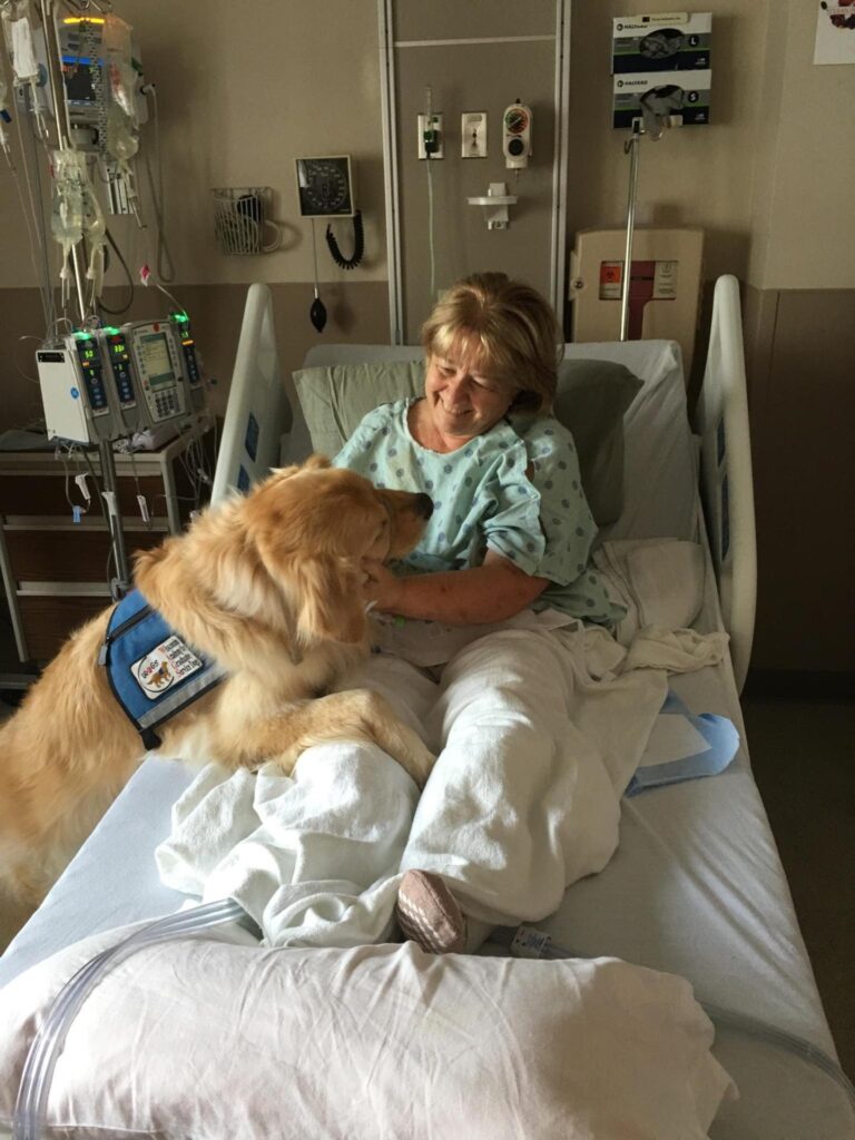 Woman smiling in hospital bed being comforted by a WAGS dog.